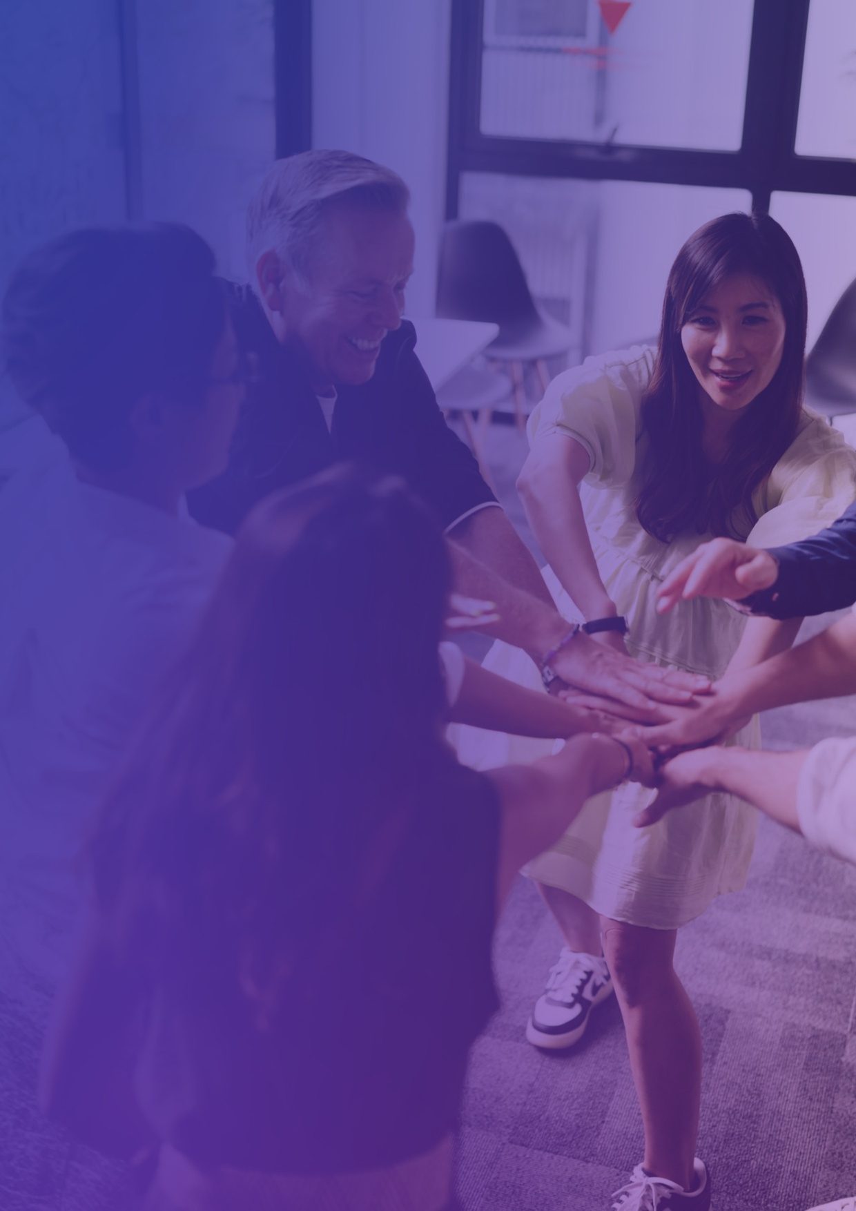 A group of colleagues laughing as they stack their hands together in the middle of a circle